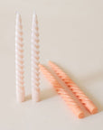 Pair of two ivory, twisted taper candles with white wicks stand beside each. Beside them lay two pastel candles of the same shape laying besides.