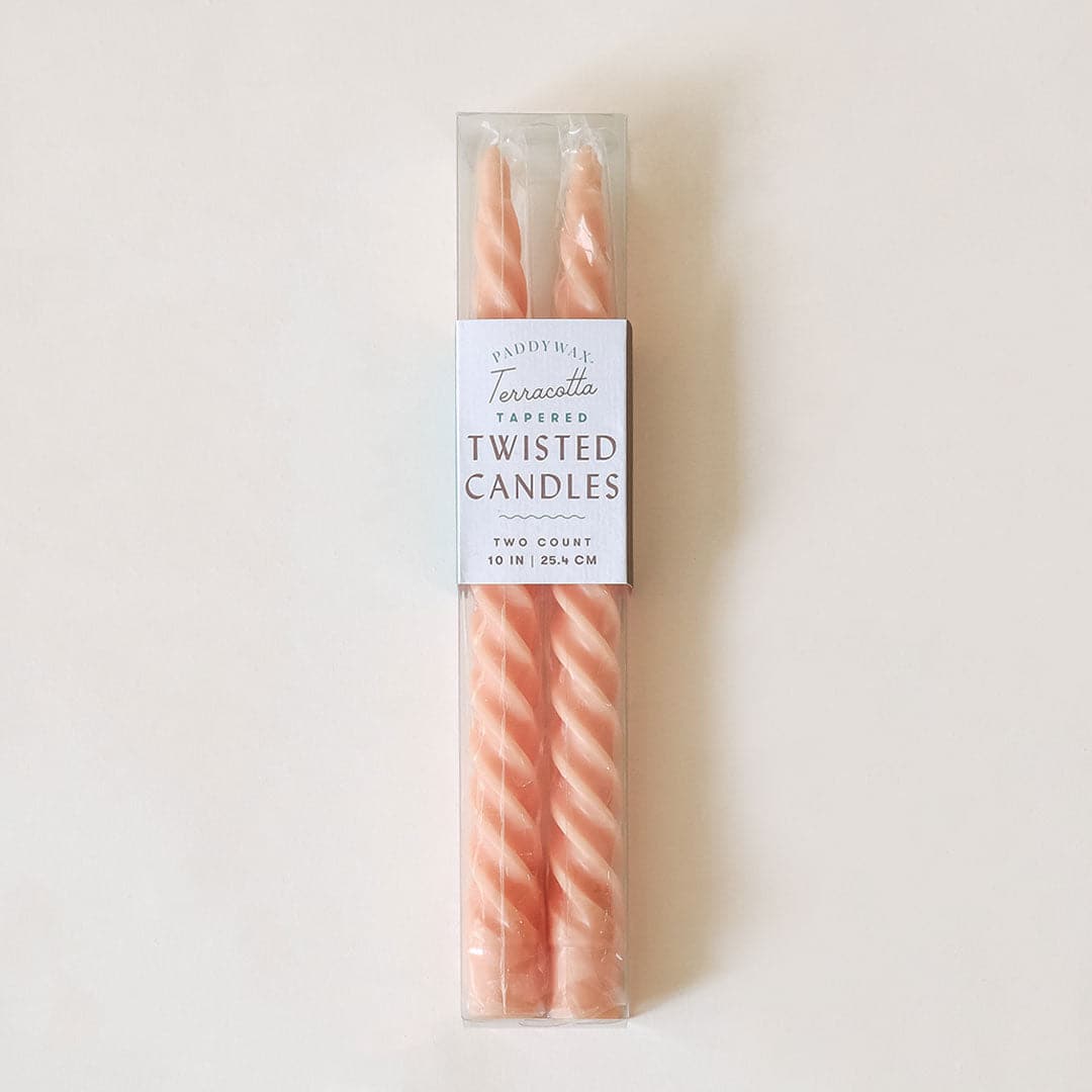 Pair of two pastel pink, twisted taper candles with white wicks are positioned beside each other in clear plastic packaging. The packaging is taped &#39;Terracotta Tapered Twisted Candles&#39;. 