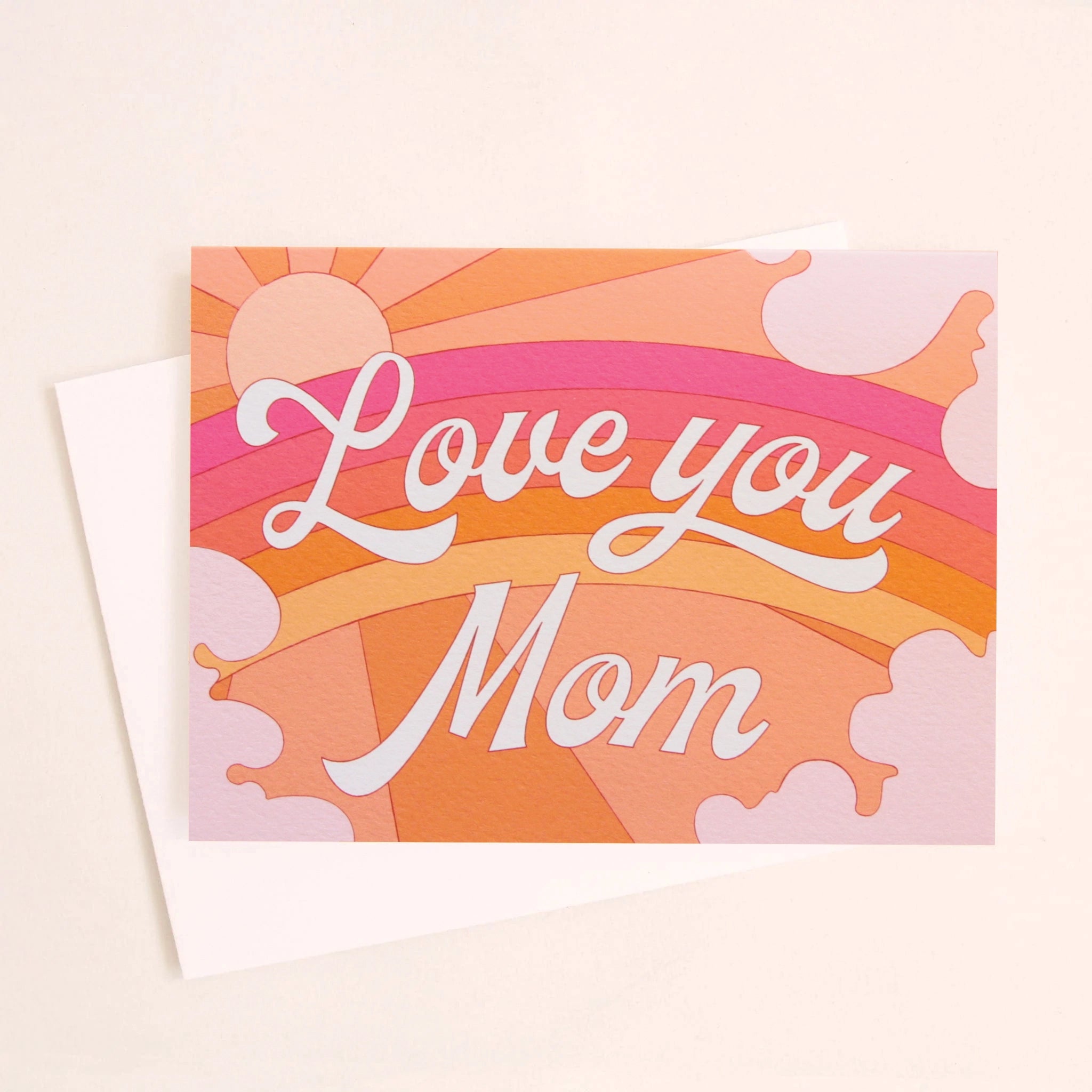 A card with a rainbow graphic made with shades or orange, pink and red along with a shining sun, subtle clouds around the edge and white cursive text that reads, &quot;Love you Mom&quot; in the center as well as a white envelope.