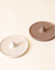 Two separate incense holders. They have a circular shape with a point in the center that is raised with a hole to place your incense in. There is a creamy white and a brown option.