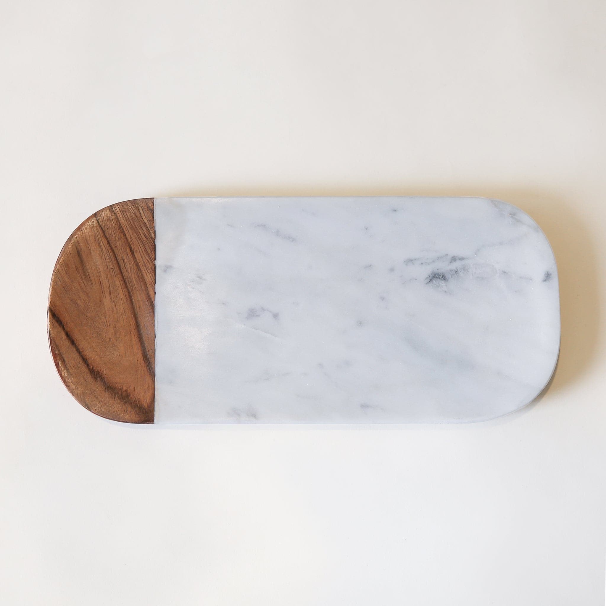 In front of a white background is an oval shaped cutting board. The cutting board is white and gray marble. The end of the left side is dark wood. 