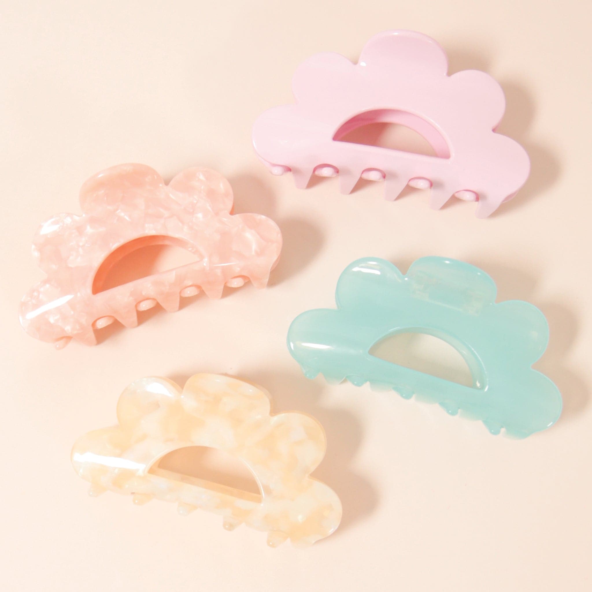 Four different colored scalloped claw clips. There is an ivory, a pink, a scallop and then a light blue.