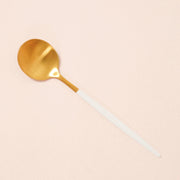 On a tan background is a white handled brass planting spoon.