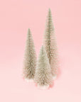three silver bristle tress of varying heights on a pink background