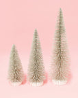 three silver bristle tress of varying heights on a pink background