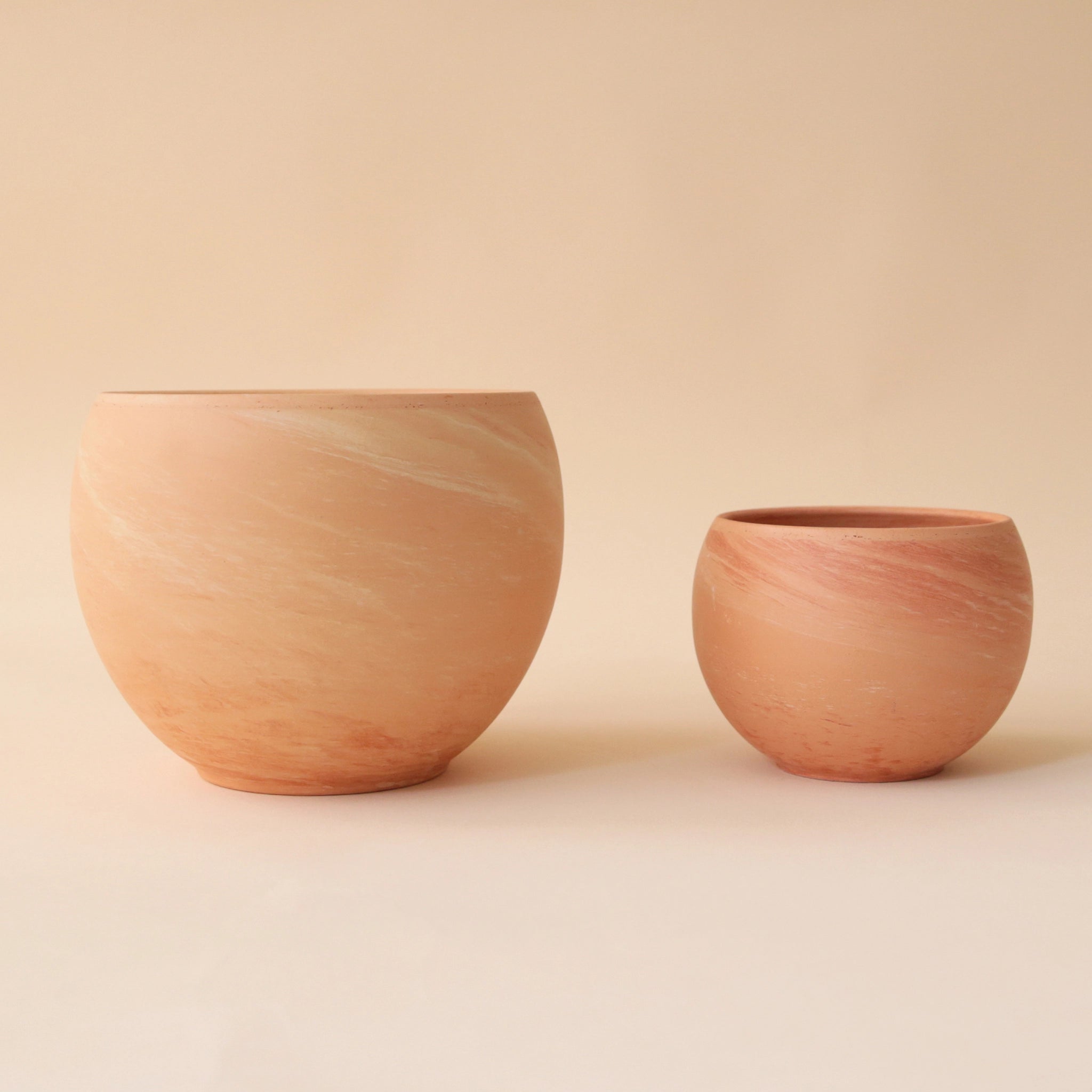 On a peach background is two round terracotta planters in two different sizes. 