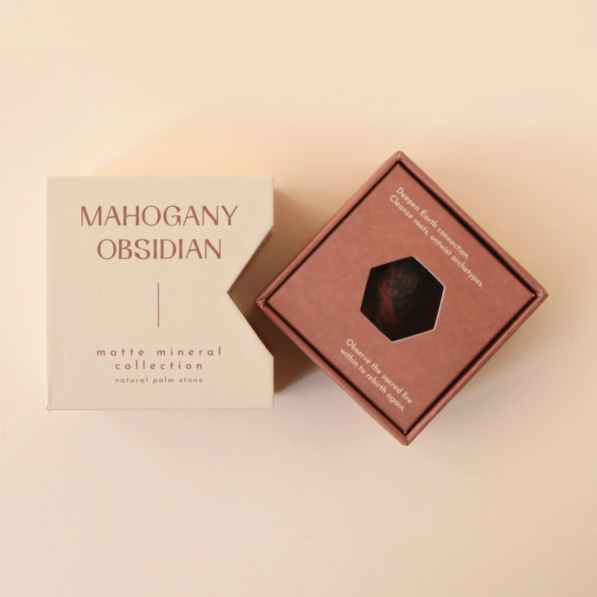 A tan box that reads, &quot;Mahogany Obsidian Matte Mineral Collection&quot; in dark red letters along with a round obsidian stone in front of it that features black and dark red coloring. Keep in mind, each stone is unique and may vary slightly in color and shape.