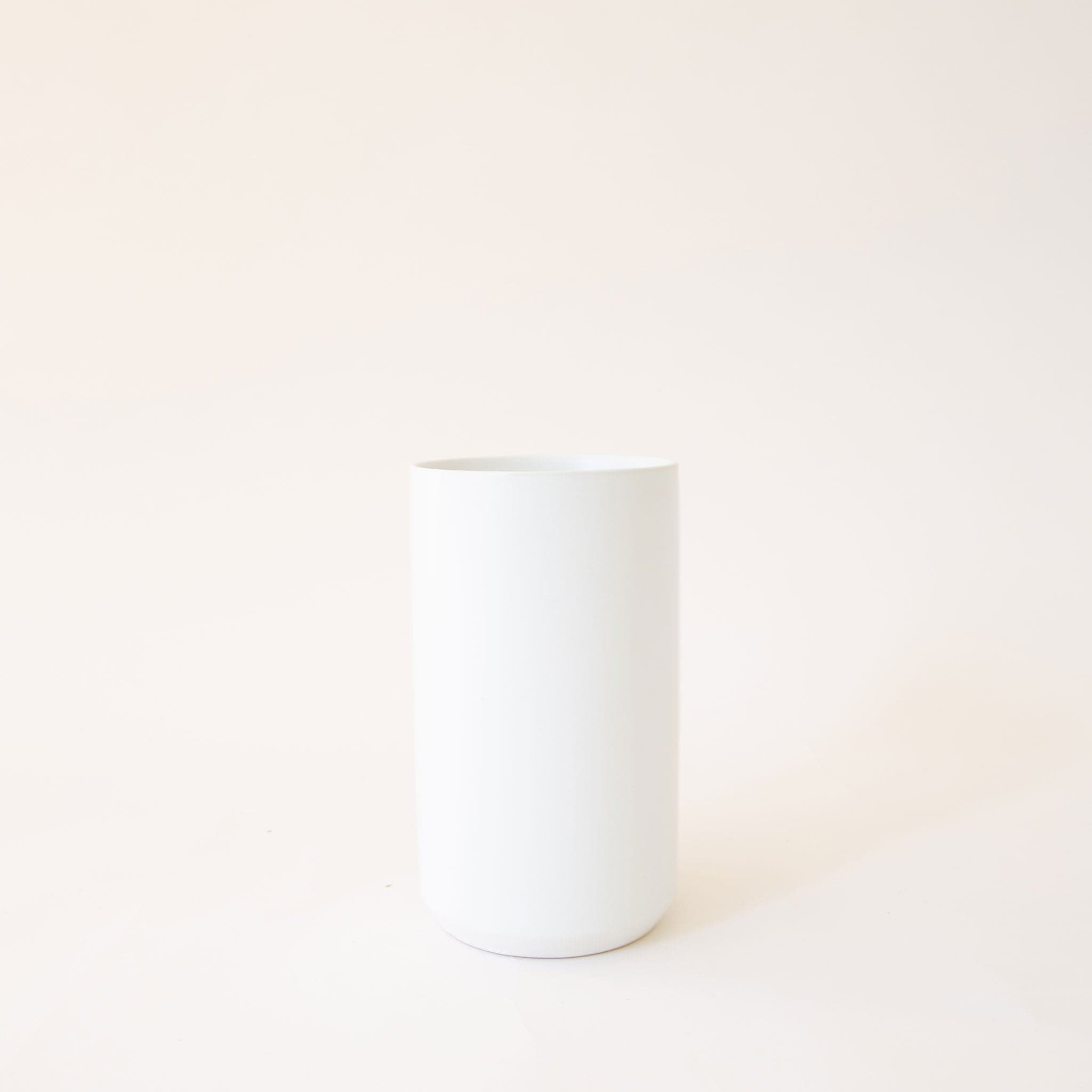 Narrow white cylinder vase. The vase lays against a blush pink background.