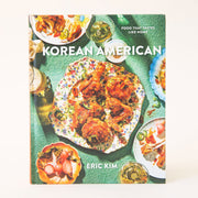 Hard cover cookbook titled 'Korean American' in white bold lettering. The cover is filled with colorful dishes of beautifully curated meals. The plates lay against a sea green textured background. 