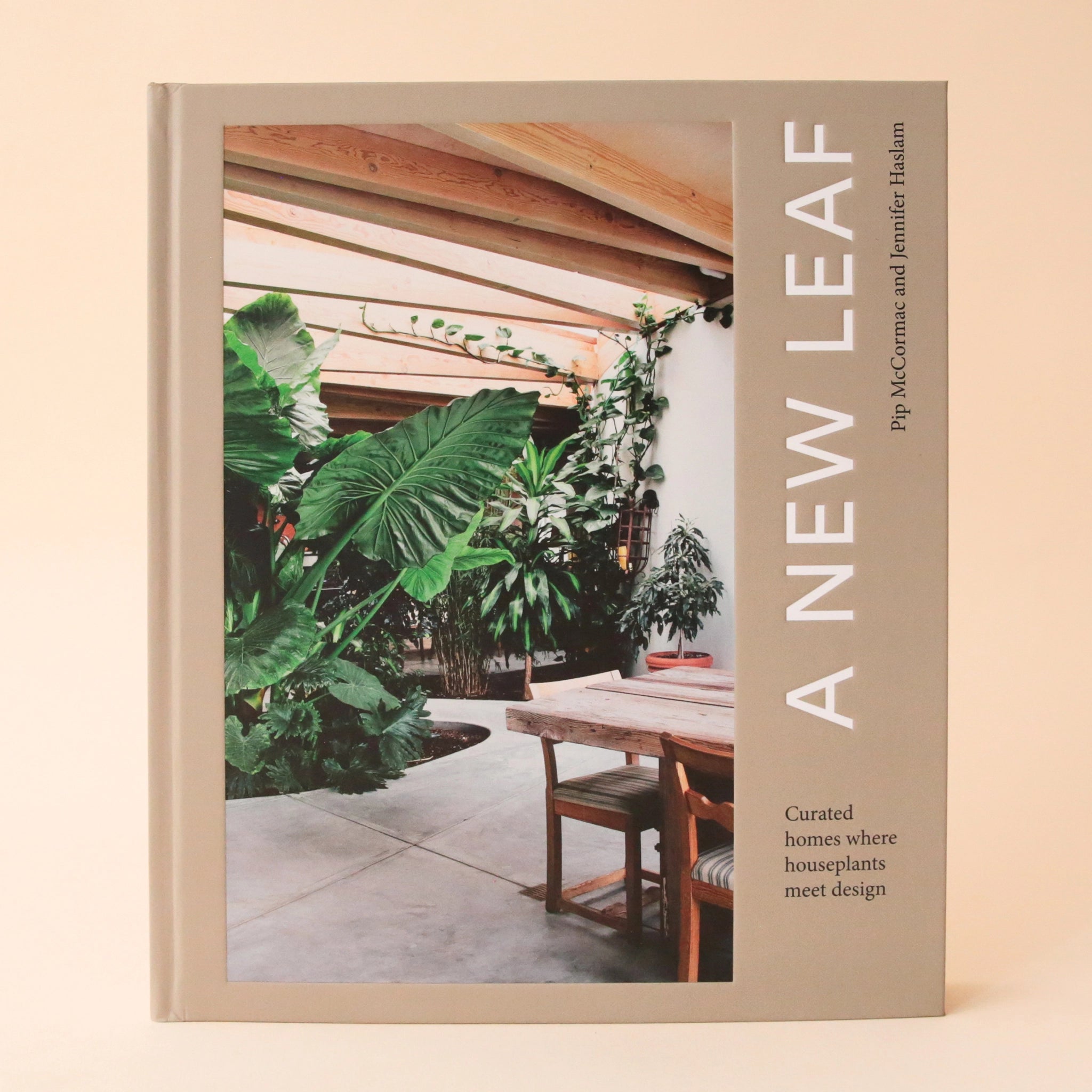 A neutral tan book cover with a photograph of a home with tons of greenery along with sideways white text that reads, &quot;A New Leaf Curated homes where houseplants meet design&quot;.