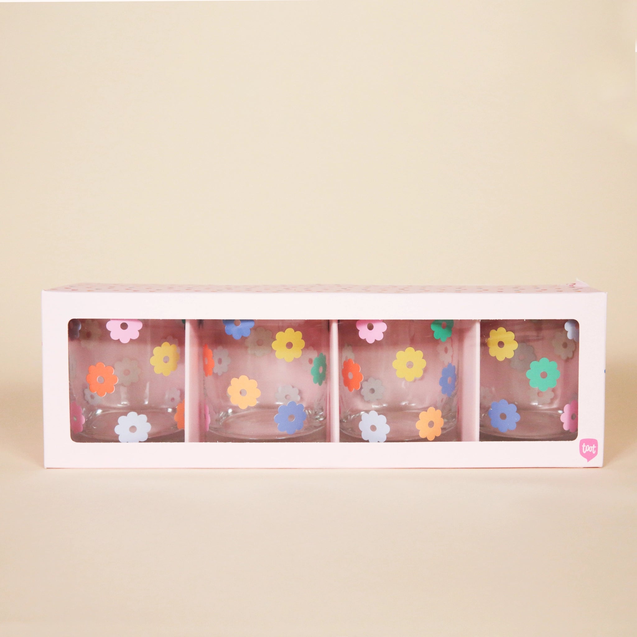 A set of four short glass tumblers with multicolor daisy pattern photographed here in the light pink box they come in.