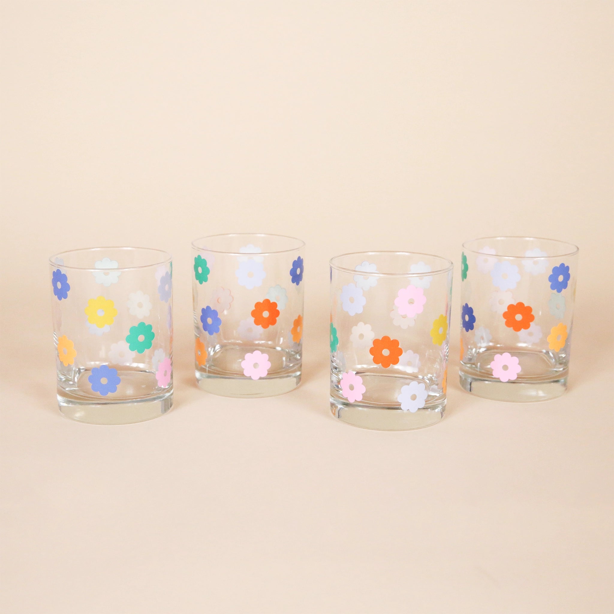A set of four short glass tumblers with multicolor daisy pattern.