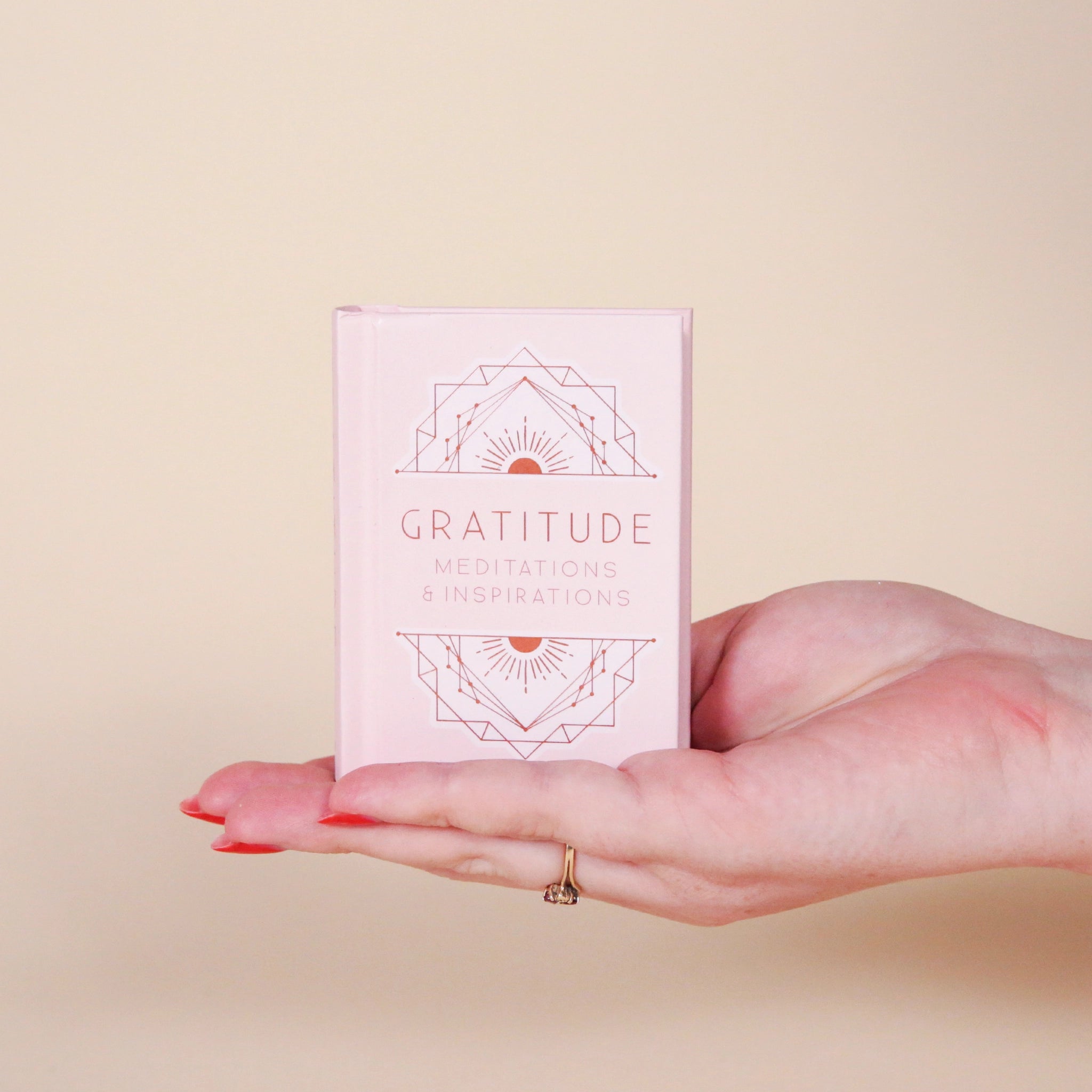 A small pink book that says, &quot;Gratitude Meditations &amp; Inspirations&quot; in light pink on the front cover as well as s geometric illustration above and below the text. 