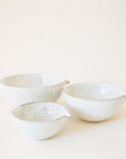 A set of three ceramic bowls nested inside one another. They feature a white base, glossy finish and a tan/brown speckled design. They are rounded bowls with a 'v' shaped design on two of the sides making them ideal for pouring if needed.