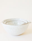 A set of three ceramic bowls nested inside one another. They feature a white base, glossy finish and a tan/brown speckled design. They are rounded bowls with a 'v' shaped design on two of the sides making them ideal for pouring if needed.