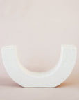 Modern ceramic u-shaped candle holder, designed to hold two candle sticks on each end. This white candle stand with faint speckles lays against a soft toned background.