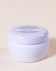 A small lavender tin candle with white wax and a white diamond repeating pattern on the outside of the tin. Comes with a matching purple lid that reads, "Capri Blue Volcano".