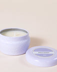 A small lavender tin candle with white wax and a white diamond repeating pattern on the outside of the tin. Comes with a matching purple lid that reads, "Capri Blue Volcano".
