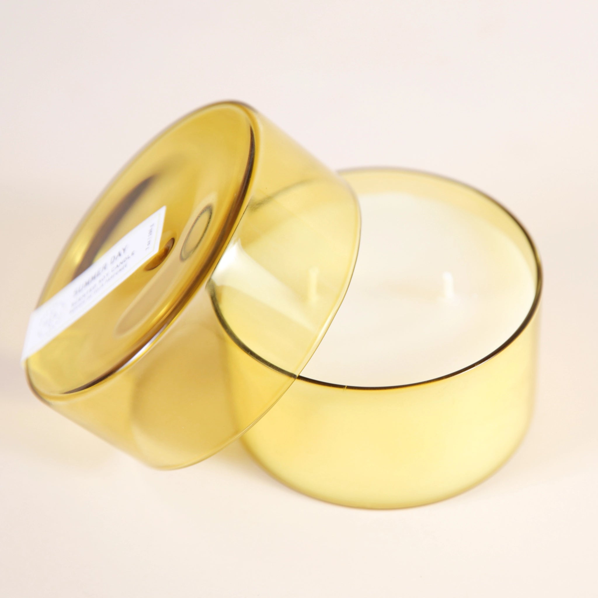 On a cream background is a yellow glass candle with a white double wick candle inside along with a coordinating yellow glass lid. 
