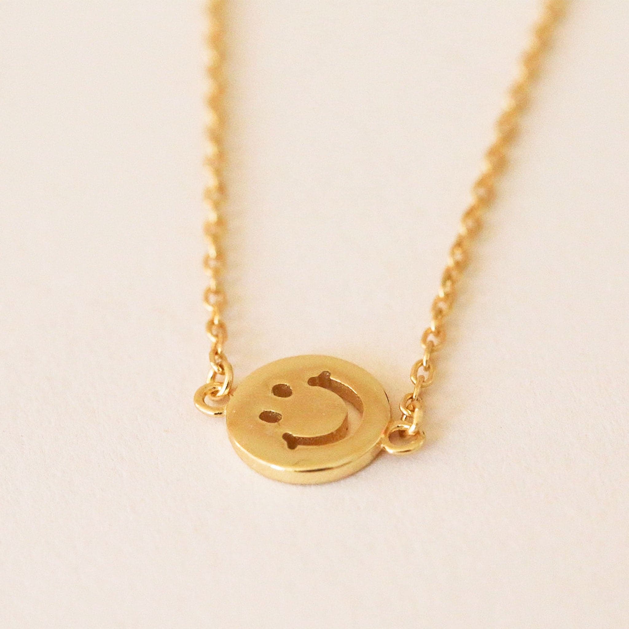 Gold chain necklace complete with classic smiley face pendant turned sideways. The pendent is connected to the chain by two loops on each side.