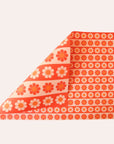 Sheet of wrapping paper filled with stripes of bright and pastel orange flowers. The sheet is bent forward, revealing the other side of the wrapping paper. The back side is covered in larger stripes of the same floral print.
