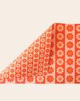 Sheet of wrapping paper filled with stripes of bright and pastel orange flowers. The sheet is bent forward, revealing the other side of the wrapping paper. The back side is covered in thinner stripes of the same floral print.