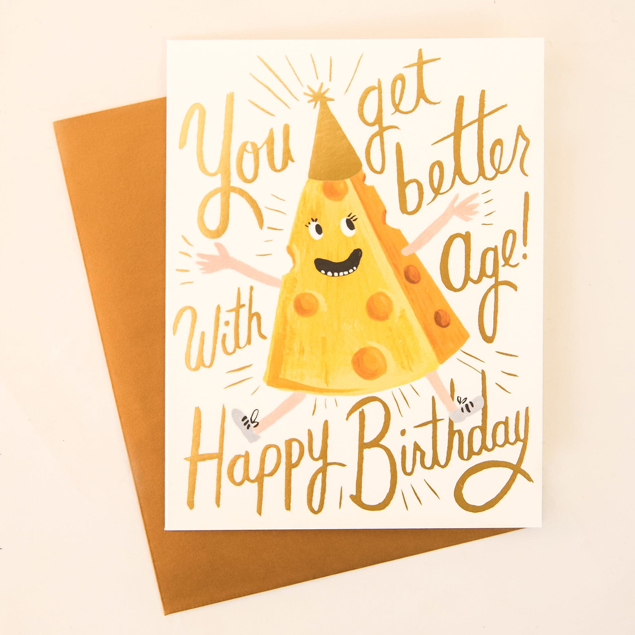 A white card with a yellow slice of cheese with a smiling face and birthday hat along with cursive writing that reads, "You get better with age! Happy Birthday".