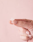On a light pink background is a model holding a tiny rose quartz crystal in the shape of a mushroom.