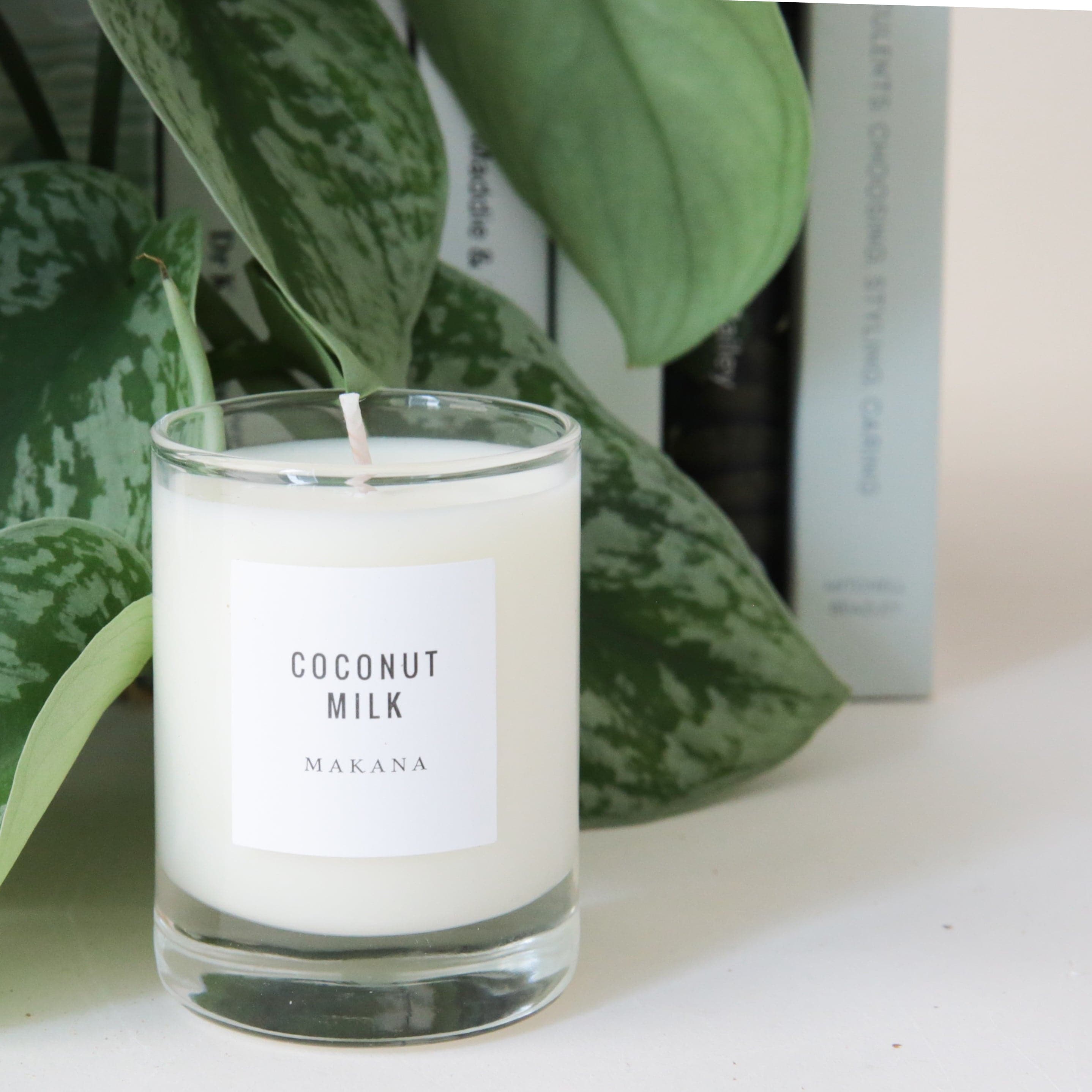 A clear glass jar candle with white wax and a white square label that reads, &quot;Coconut Milk Makana&quot; in clean black text.
