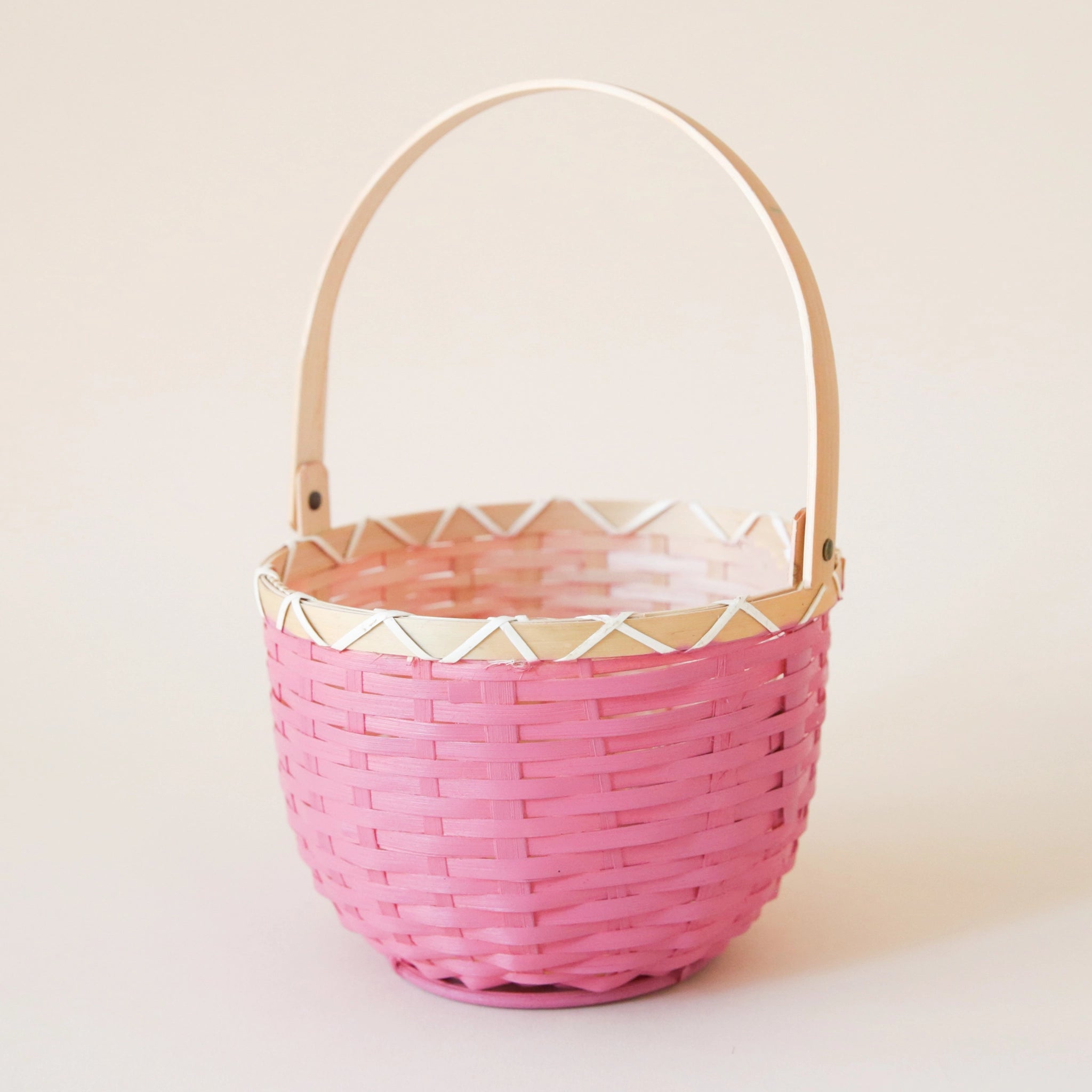 On a cream background is a bright pink and natural rattan woven spring basket. 