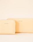 On a cream background is a light yellow zip wallet with silver detailing and "Matt & Nat" written tiny on the front of the wallet, photographed with a smaller square shaped wallet.