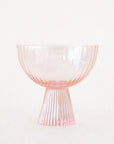 On a white background is a ribbed light pink coupe glass.