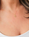 A dainty gold chain necklace with a gold circle pendant in the center with a cut out of a daisy flower, photographed being worn on a model.