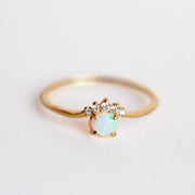 In front of a white background is a gold ring. On the front is a round white opal with five white stones on the top of the opal.