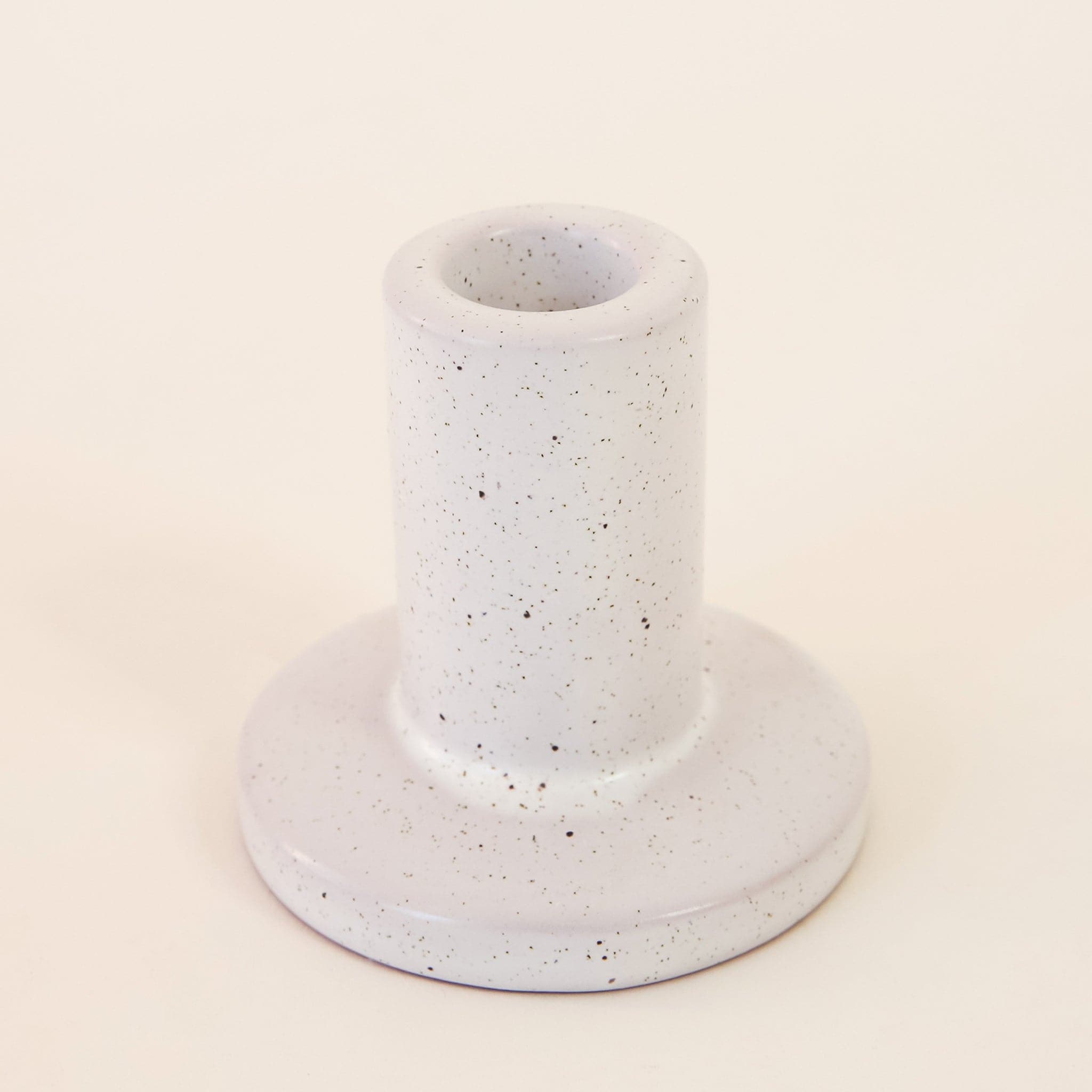 Against a white background is a gray, ceramic candle holder with black speckles on it. The base is round with a tall, cylinder top. 