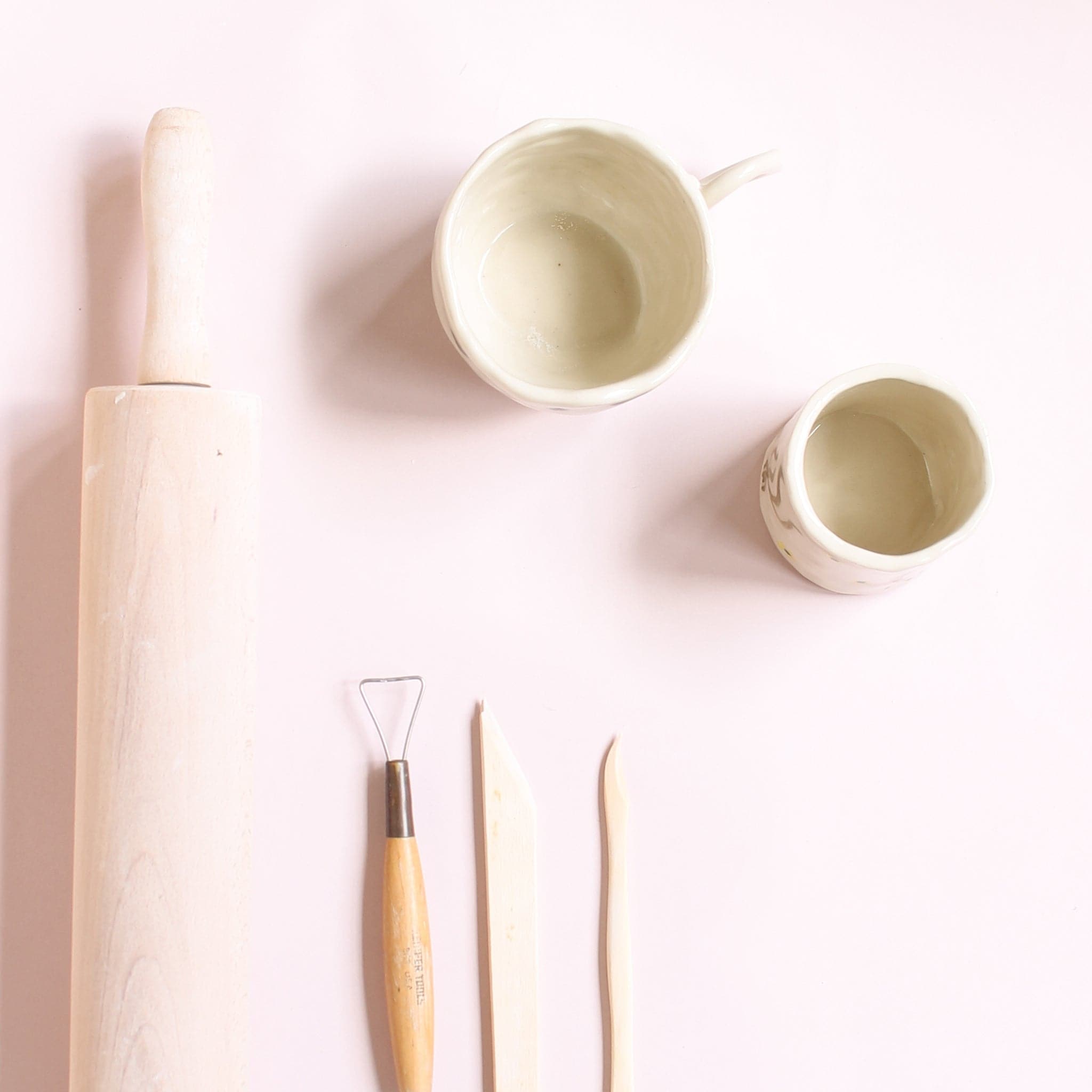 On a light pink background is two clay creations next to a rolling pin and modeling tools. 