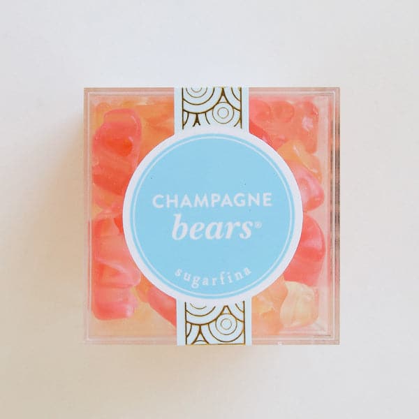 A clear acrylic box filled with light pink and champagne colored gummy bears along with a blue circle label with text that reads, "Champagne Bears Sugarfina".