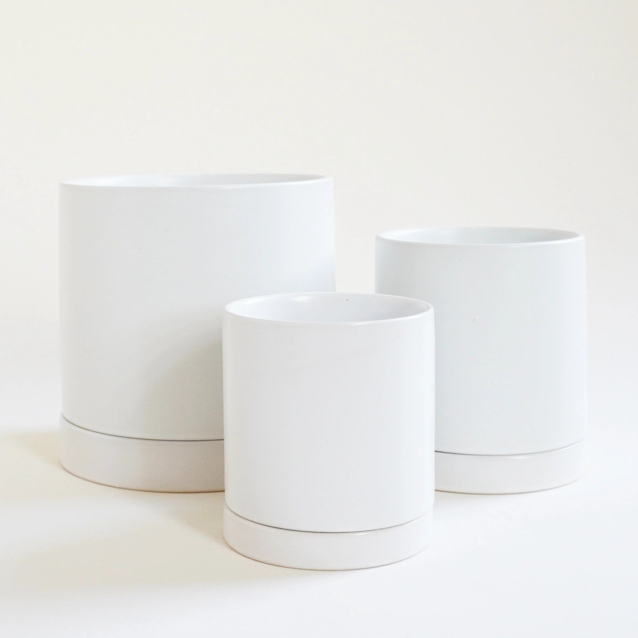 a small, medium, and large simple white pot with matching saucer all sit on a white ground