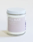 A clear glass jar candle with a light lavender label with white text that reads, "Del Mar" and a white lid.