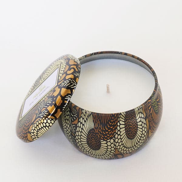Round tin candle vessel and lid with dark and light gold floral pattern and white wax candle.