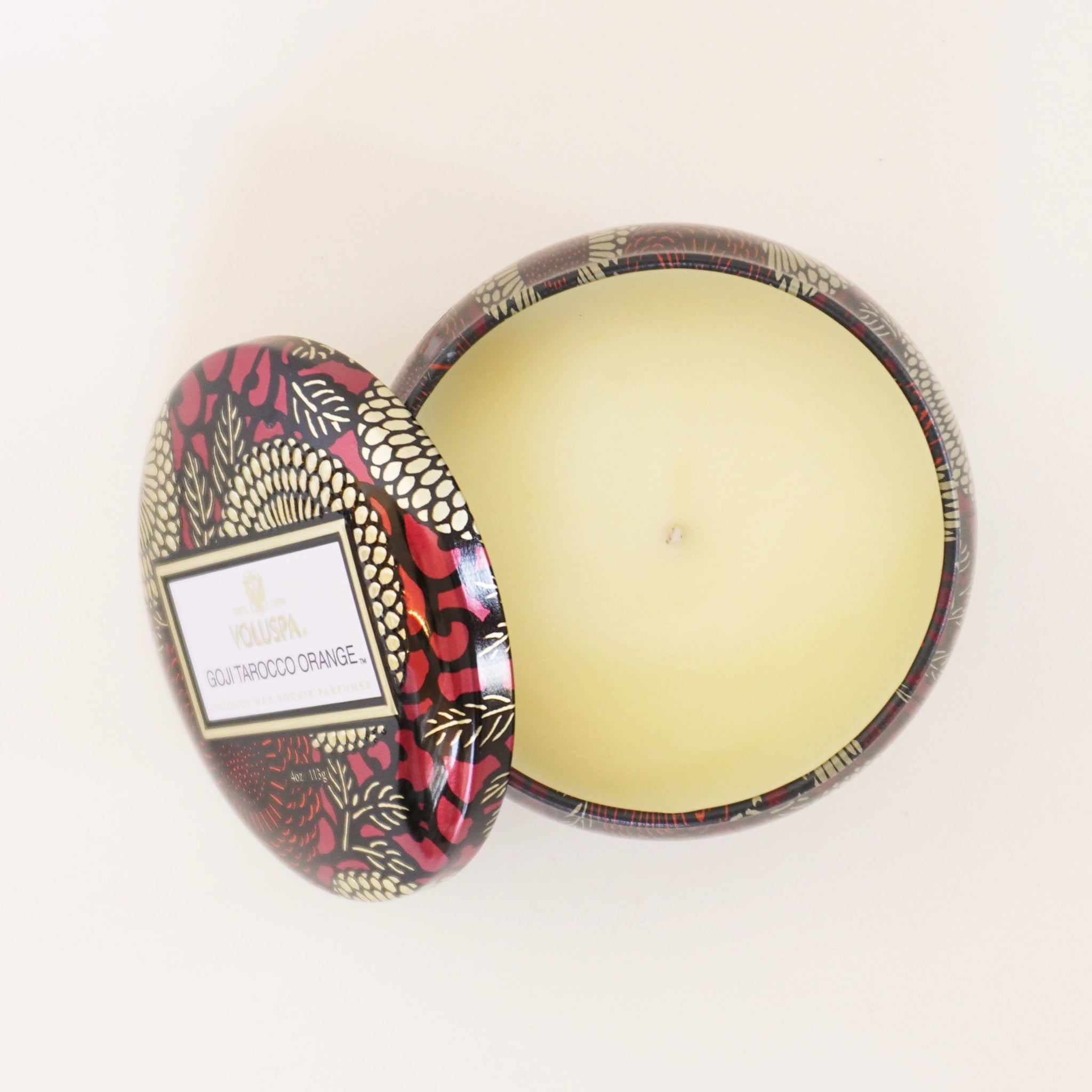On a white background is a red tin with a single wick candle inside and a label on the lid that reads, &quot;Voluspa Goji Torocco Orange&quot;.