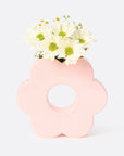 A light pink ceramic vase in the shape of a daisy with an opening in the center and an opening at the top to insert plants and floral stems.