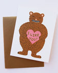 A white folded card with a brown bear graphic on the front holding a pink heart that says, "I Like You" in black writing.