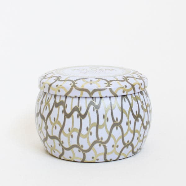 Against a white background is the side view of a round tin candle with a matching lid. The candle and the lid are white with a gold and silver design. 