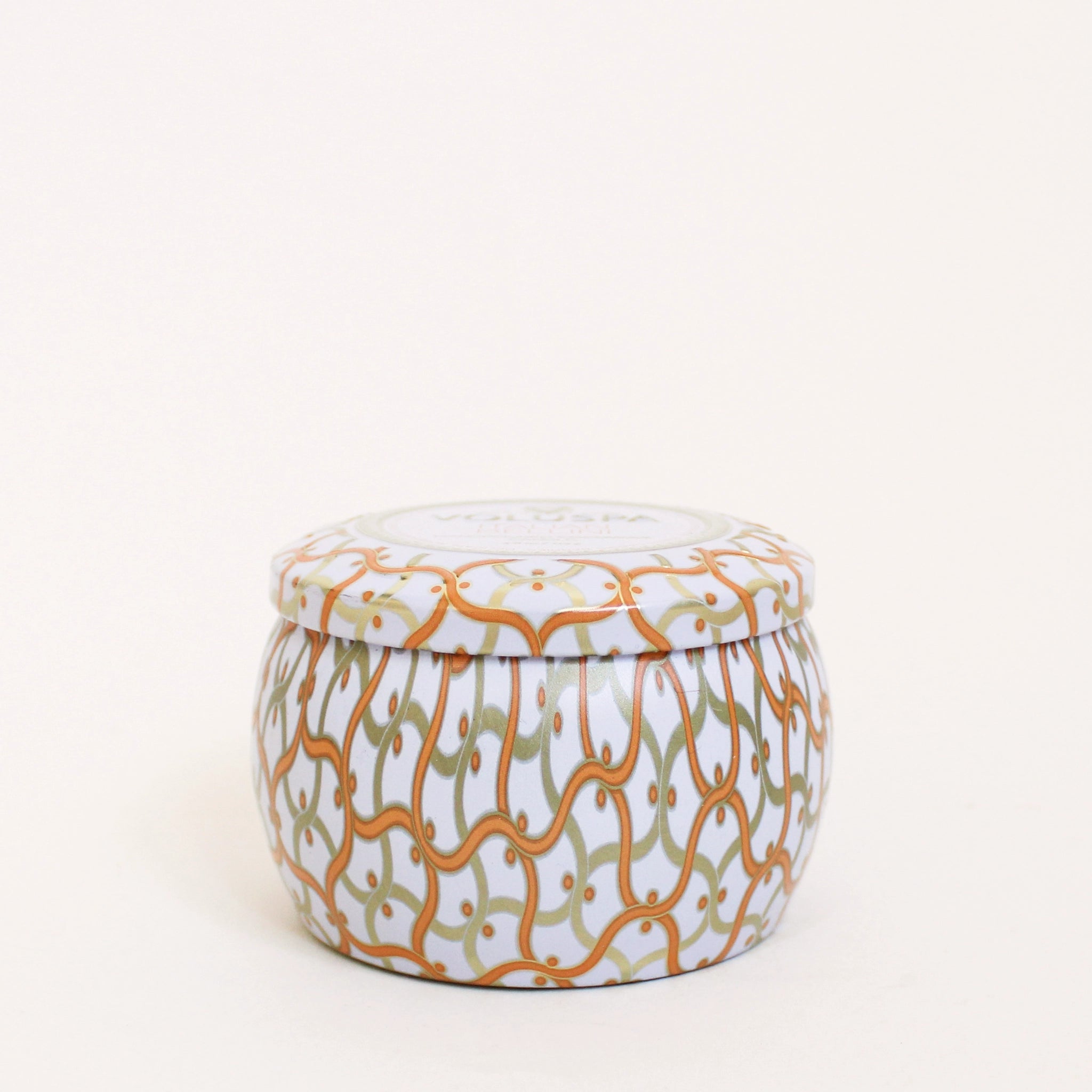 On a cream background is a orange and white tin that contains a candle along with a circle label in the center of the lid that reads, &quot;Voluspa Italian Bellini&quot;.