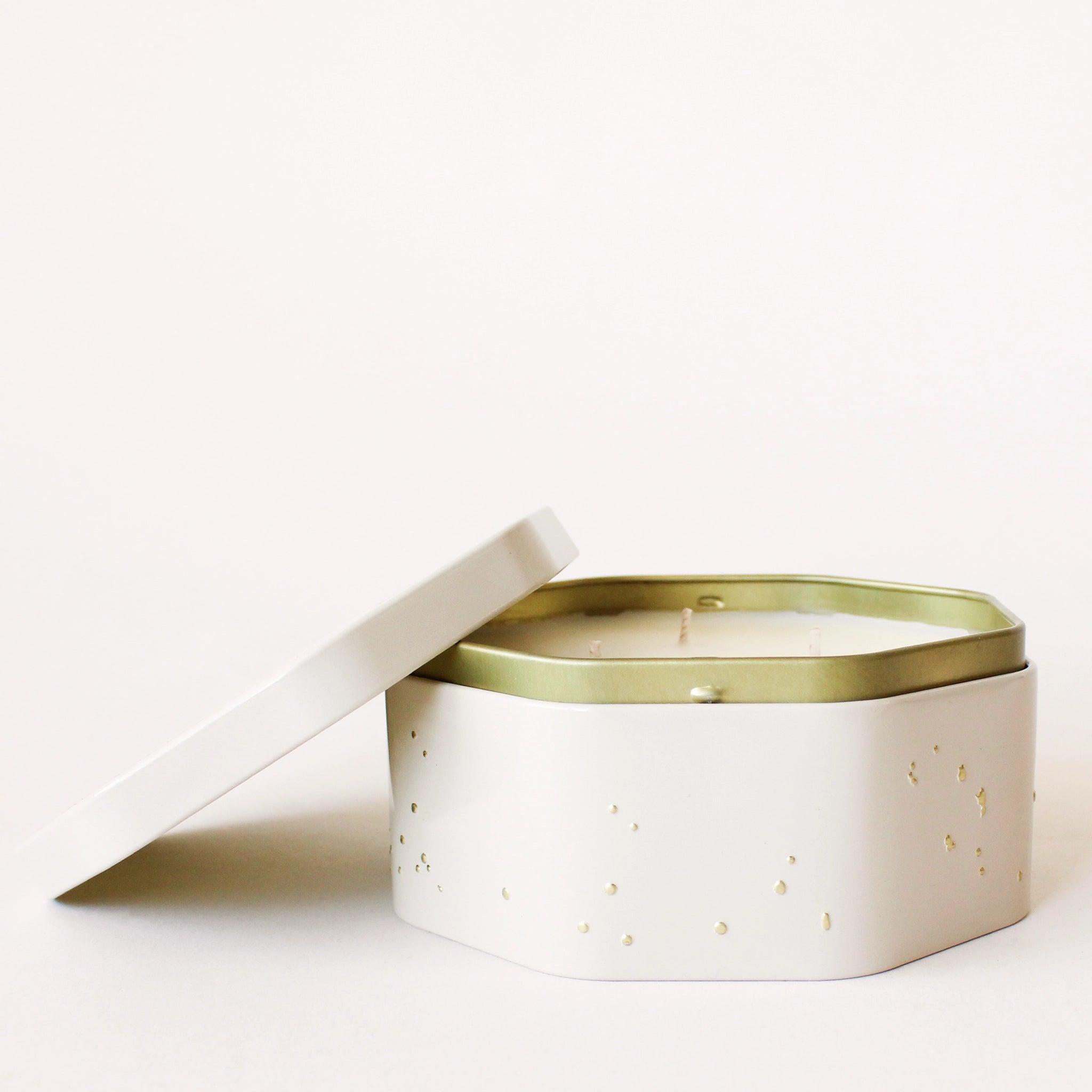 On a white background is an octagon tin in a white shade with a white three wick candle inside along with a label on the lid that reads, &quot;Voluspa Coconut Papaya&quot;.