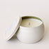 On a cream background is a round tin candle with a lid and a single wick candle inside. 