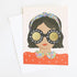 Photo of a greeting card on a white background. Card features the head and shoulders of a girl with short brown hair and tan skin with red lips on a pink background. She is wearing a blue floral headband and red shirt with floral collar. She has round black glasses that say "happy birthday, birthday girl!" on the frames. Gold foil fills in the inside of the glasses. Comes with a white envelope.