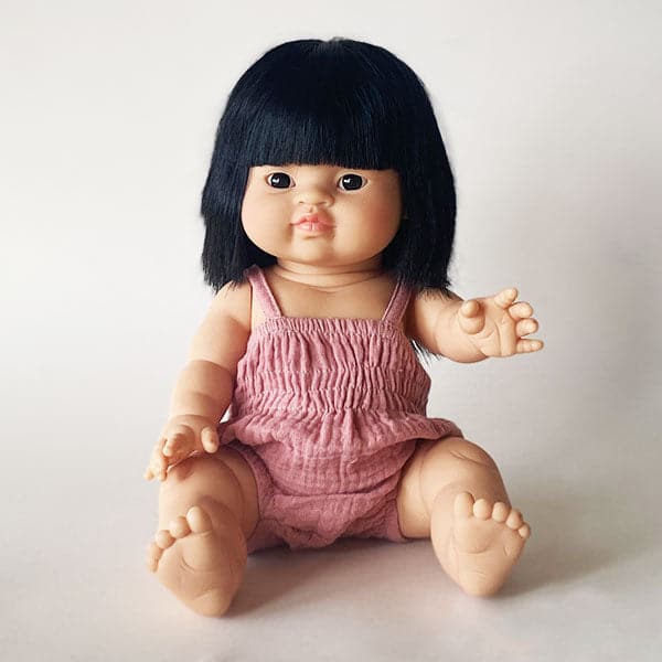 An asian baby doll with black straight hair and dressed in a pink onesie.