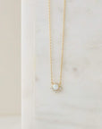 A dainty gold necklace with a round opal pendant in the center that is lined with cz stones around the bottom edge.